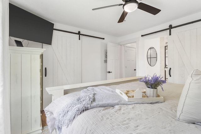 bedroom featuring a barn door, ceiling fan, and wooden walls