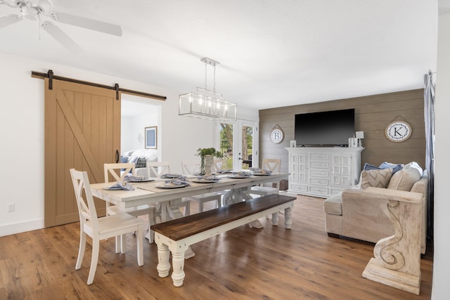 dining room with hardwood / wood-style floors, ceiling fan with notable chandelier, a barn door, and wooden walls