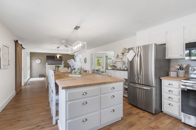 kitchen featuring appliances with stainless steel finishes, a barn door, white cabinets, butcher block countertops, and hanging light fixtures