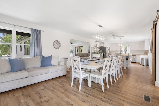 dining room with a barn door, ceiling fan, and light hardwood / wood-style floors