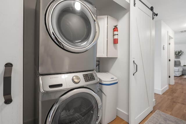 laundry room featuring a barn door, stacked washing maching and dryer, and light hardwood / wood-style floors