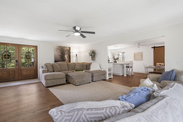 living room featuring ceiling fan with notable chandelier, a barn door, and dark hardwood / wood-style floors