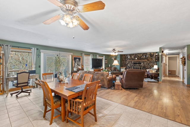 dining room featuring a stone fireplace, ceiling fan, and light hardwood / wood-style floors