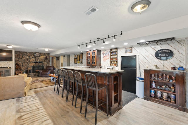 bar featuring black fridge, a textured ceiling, a fireplace, light hardwood / wood-style floors, and wood walls