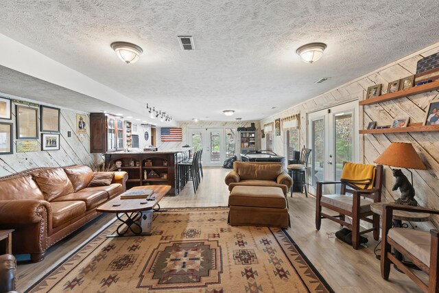 living room featuring french doors, light wood-type flooring, and wood walls