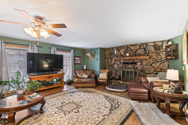 living room featuring wood-type flooring, a stone fireplace, and ceiling fan