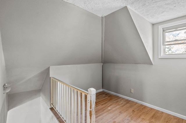 additional living space with a textured ceiling, light hardwood / wood-style flooring, and lofted ceiling