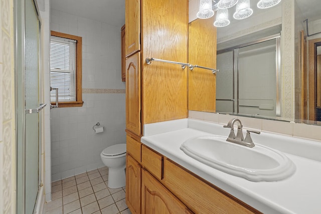 bathroom featuring tile patterned floors, toilet, vanity, a shower with shower door, and tile walls