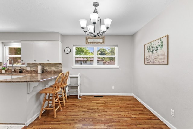 kitchen with white cabinets, decorative light fixtures, an inviting chandelier, and light hardwood / wood-style flooring