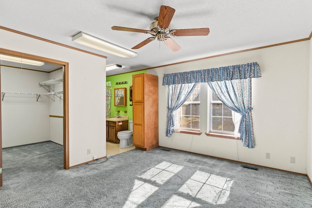 unfurnished bedroom with connected bathroom, ceiling fan, light colored carpet, and a textured ceiling