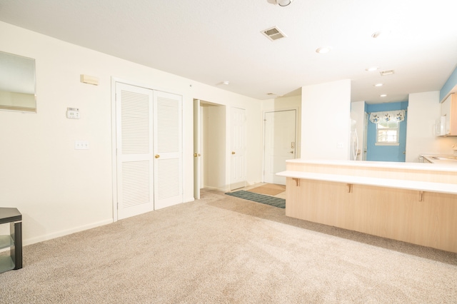 kitchen featuring kitchen peninsula, light brown cabinetry, light colored carpet, and a breakfast bar area