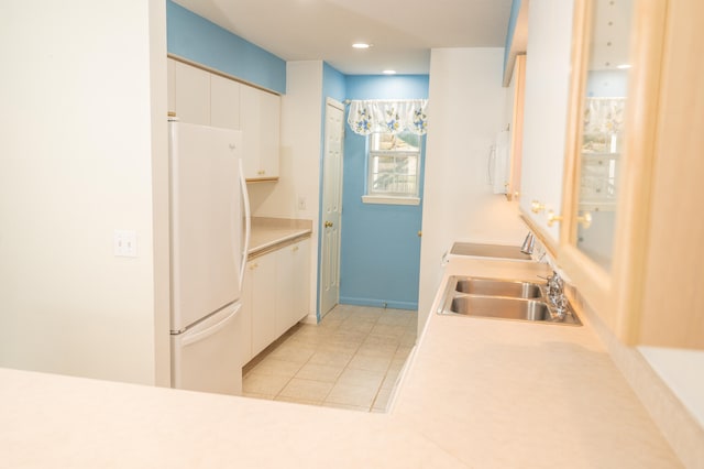 kitchen with white fridge, white cabinetry, sink, and light tile patterned floors