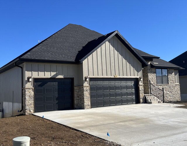 exterior space with stone siding, driveway, a garage, and roof with shingles