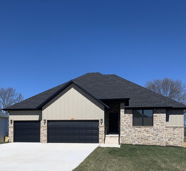 view of front of property with a garage, a front yard, board and batten siding, roof with shingles, and driveway