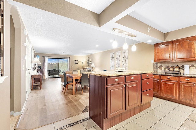 kitchen with light wood-type flooring, backsplash, a textured ceiling, pendant lighting, and a center island