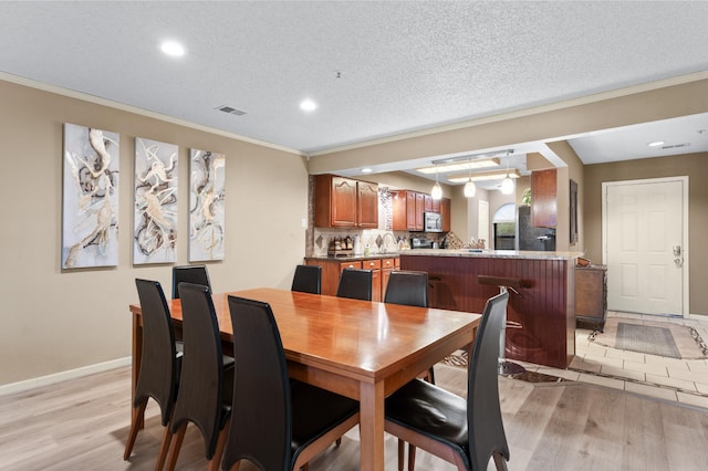 dining room with a textured ceiling, light wood-type flooring, crown molding, and sink