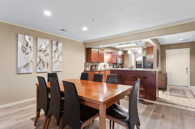 dining area featuring sink, light wood-type flooring, a textured ceiling, and ornamental molding