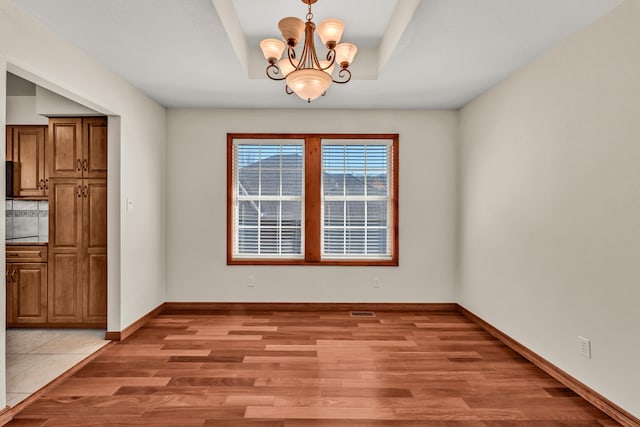 unfurnished dining area featuring a tray ceiling, light hardwood / wood-style flooring, and a chandelier