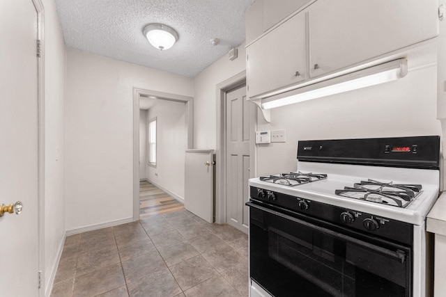 kitchen with white cabinets, light tile patterned floors, a textured ceiling, and white range with gas cooktop