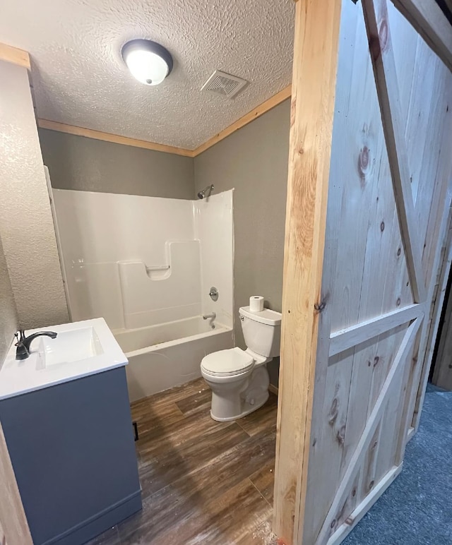 full bathroom featuring vanity, a textured ceiling, shower / washtub combination, hardwood / wood-style floors, and toilet