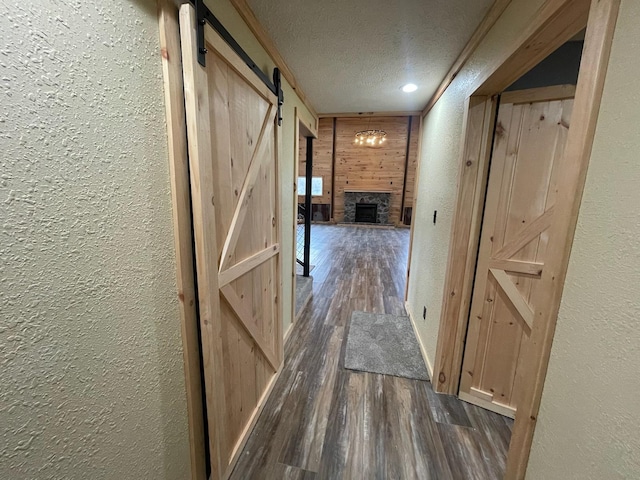 corridor featuring wood walls, a barn door, a textured ceiling, and dark wood-type flooring