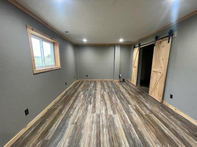 unfurnished bedroom featuring a barn door, ornamental molding, and dark wood-type flooring