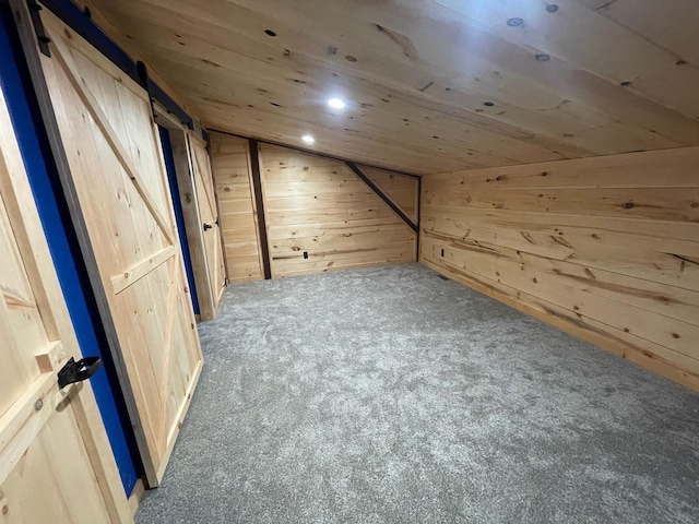 additional living space with a barn door, wood walls, carpet, and lofted ceiling