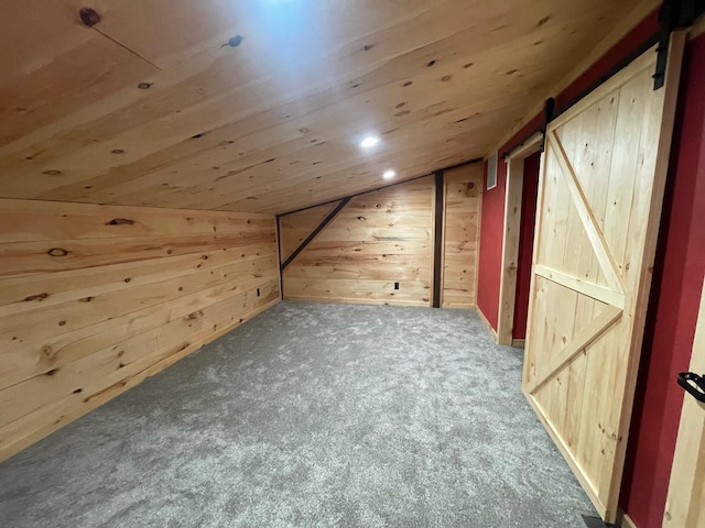 bonus room with carpet flooring, a barn door, wooden walls, and vaulted ceiling