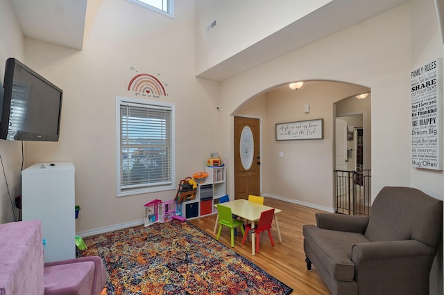 recreation room with hardwood / wood-style floors and a towering ceiling