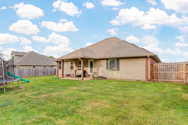 back of property featuring a patio area, a yard, and a trampoline