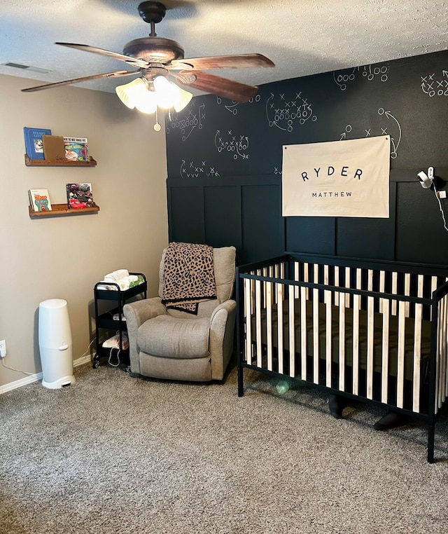 bedroom with carpet flooring, a textured ceiling, a nursery area, and ceiling fan