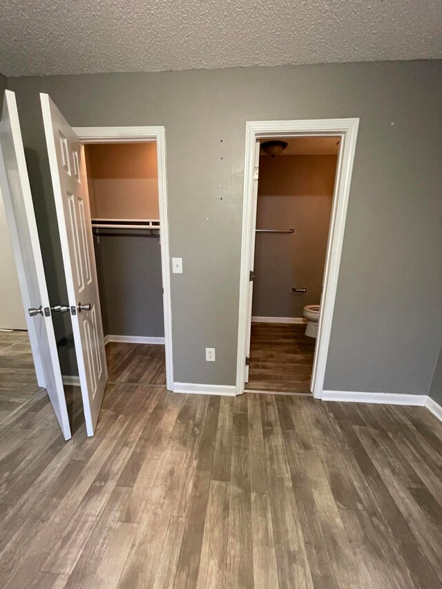 unfurnished bedroom with hardwood / wood-style floors, ensuite bath, a spacious closet, a textured ceiling, and a closet