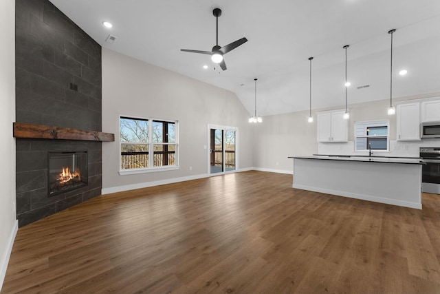 unfurnished living room featuring ceiling fan, dark wood-style flooring, a tiled fireplace, and baseboards