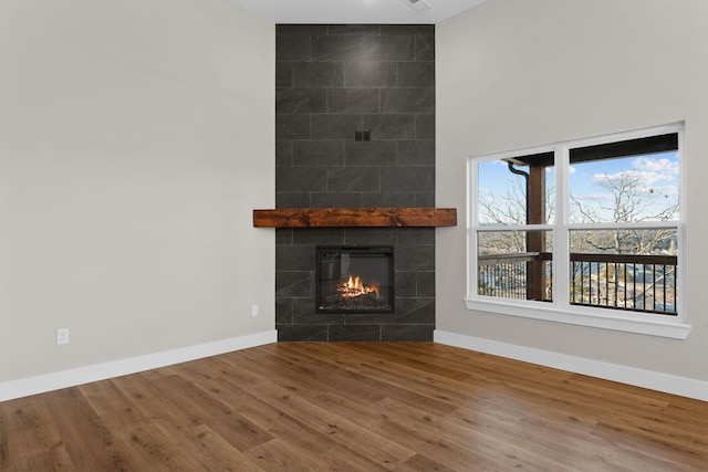 unfurnished living room with wood finished floors, a tile fireplace, and baseboards