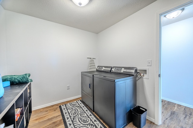 clothes washing area with washing machine and clothes dryer, light hardwood / wood-style floors, and a textured ceiling