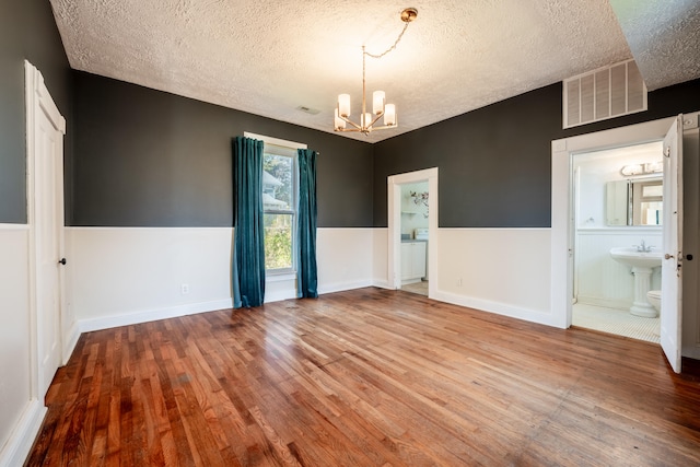 empty room featuring hardwood / wood-style floors, a textured ceiling, and a notable chandelier