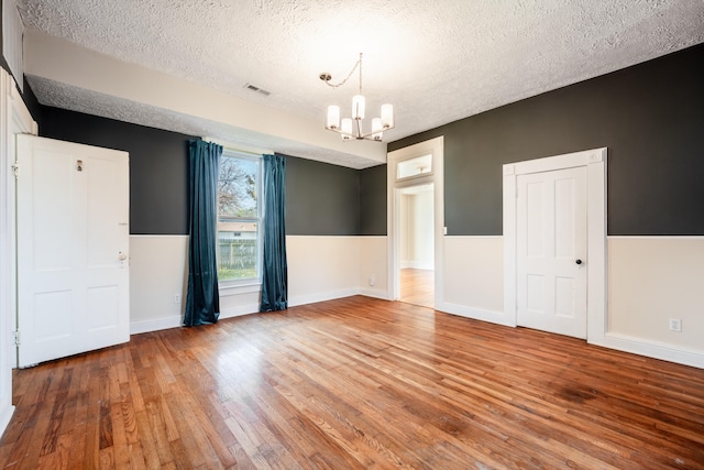 empty room with hardwood / wood-style floors, a notable chandelier, and a textured ceiling