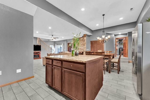 kitchen featuring a center island, light stone counters, stainless steel fridge, pendant lighting, and ceiling fan with notable chandelier