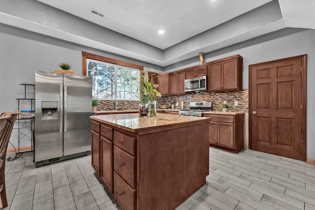 kitchen featuring decorative backsplash, appliances with stainless steel finishes, light wood-type flooring, light stone countertops, and a center island