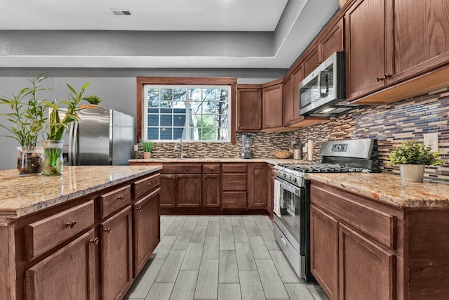 kitchen featuring appliances with stainless steel finishes, tasteful backsplash, light stone counters, and light hardwood / wood-style floors