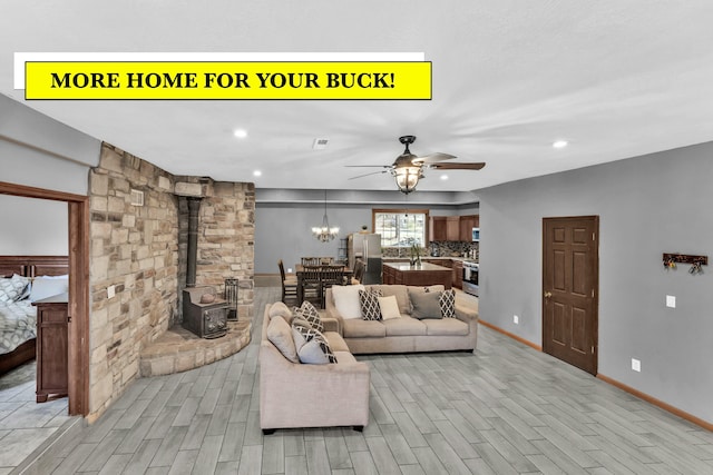 living room with ceiling fan with notable chandelier, light hardwood / wood-style flooring, and a wood stove