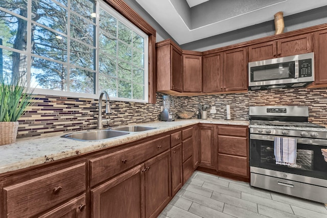 kitchen featuring decorative backsplash, stainless steel appliances, light stone countertops, and sink