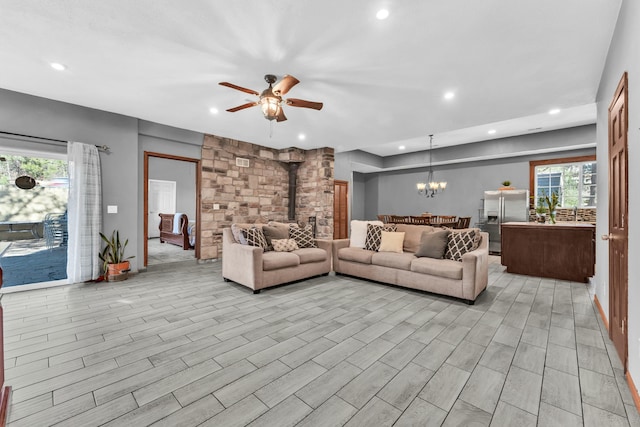 living room with a wood stove, light hardwood / wood-style floors, and ceiling fan with notable chandelier