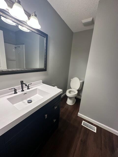 bathroom featuring walk in shower, vanity, a textured ceiling, hardwood / wood-style flooring, and toilet