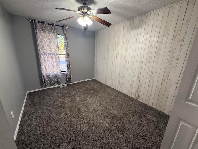 carpeted empty room with a textured ceiling, ceiling fan, and wood walls