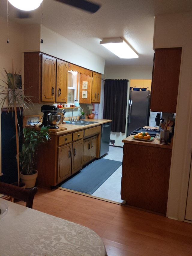 kitchen with stainless steel appliances, ceiling fan, sink, and light hardwood / wood-style floors