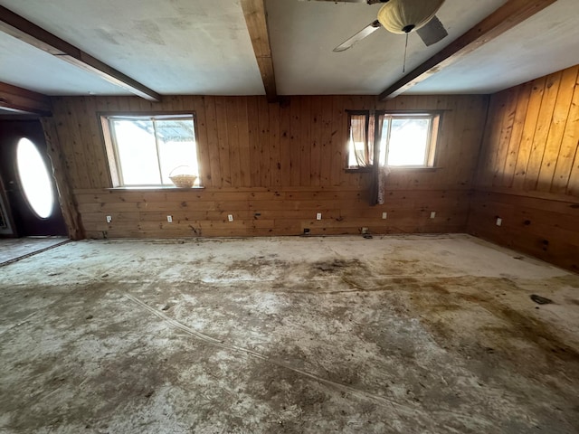 unfurnished room featuring beam ceiling, a wealth of natural light, wooden walls, and ceiling fan