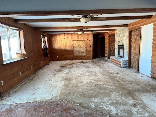 unfurnished living room featuring beamed ceiling, ceiling fan, a stone fireplace, and wooden walls