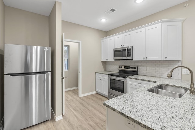 kitchen featuring white cabinets, appliances with stainless steel finishes, sink, light stone counters, and light hardwood / wood-style flooring