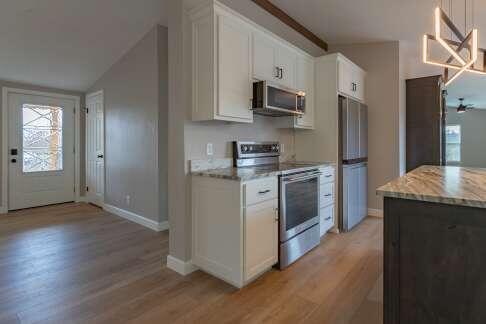 kitchen featuring vaulted ceiling, light hardwood / wood-style flooring, stainless steel appliances, light stone countertops, and white cabinets